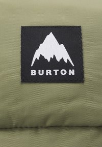 Tissu vert olive avec une finition texturée, comportant un patch rectangulaire noir affichant un logo de montagne blanche et "BURTON" en lettres blanches.