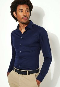 Marineblauw overhemd met lange mouwen en een button-down kraag, gemaakt van gladde stof, met contrasterende knopen, gecombineerd met lichte beige broek en een riem.