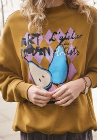 Felpa marrone con grafica colorata composta da elementi blu e beige e testo nero. Polsini a costine e vestibilità rilassata.