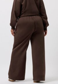 Braune weite Sweatpants aus weichem Material, mit elastischem Bund und lockerem Schnitt, sowie feinen Textur- und Nähedetails.