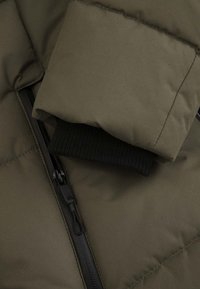 Zielona oliwkowa kurtka puchowa z suwakiem, czarnymi ściągaczami na rękawach oraz pikowaną teksturą na rękawach i korpusie dla dodatkowej izolacji.