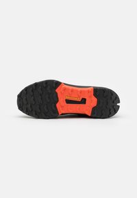 Semelle de chaussure noire avec des crans profonds, dotée d'une section centrale orange avec un logo "Continental" et des accents texturés.