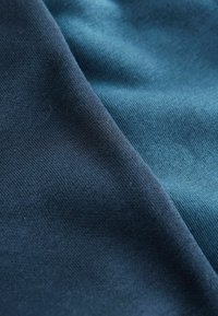 Zwei übereinanderliegende Stoffe: einer in dunklem Marineblau und der andere in Teal. Beide haben eine weiche, glatte Textur mit einem feinen Strickmuster.