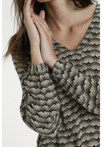 Blusa verde a fantasia con scollatura a V, dotata di un tessuto testurizzato e un design a forma di ventaglio in crema e nero. Maniche lunghe con polsini elastici.