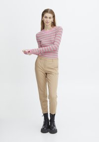 Rosa och grårandig ribbad tröja, figurnära silhuett, kombinerad med beiga kapade byxor och svarta snörstövlar. Slät textur.