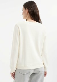 Beżowa bawełniana bluza z okrągłym dekoltem i ściągaczami. Gładka tekstura, luźny krój oraz uniwersalny design odpowiedni na codzienne noszenie.