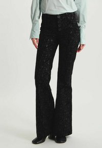 Pantalons évasés noirs avec une texture florale en sequins et une fermeture à cinq boutons à l'avant. Le tissu est brillant avec un léger éclat.