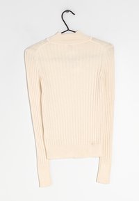 Pull beige côtelé à manches longues, col montant et ourlet ajusté. Texture douce avec des rayures verticales traversant le tissu.