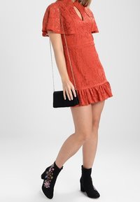 Red lace dress with short sleeves, textured fabric, a keyhole neckline, and ruffled hem; paired with black ankle boots featuring floral embroidery.