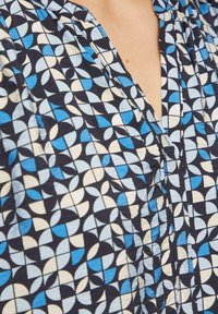 Blauwe en crèmekleurige blouse met een marineblauwe achtergrond, met een geometrisch ontwerp van overlappingen en een ontspannen halslijn.