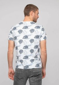T-shirt à manches courtes en bleu clair avec un motif de feuilles tropicales vert foncé. Col rond, tissu en coton doux et coupe décontractée.