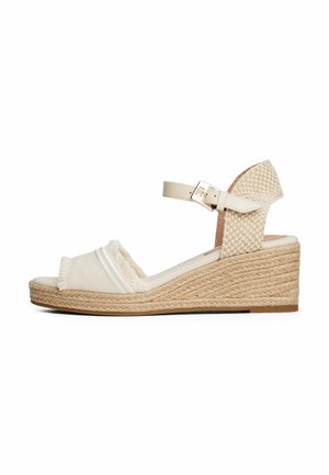 Beige kile-sandal med vævede detaljer, åben tå, ankelrem med guldbælte og platformssål med rebtekstur.
