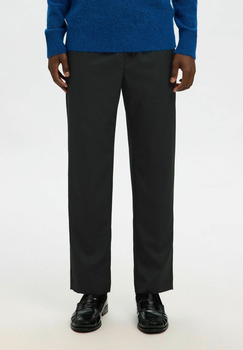 Pantaloni neri con un design a gamba dritta, realizzati in tessuto liscio. Abbinati a mocassini neri, che mostrano un aspetto pulito e minimale.
