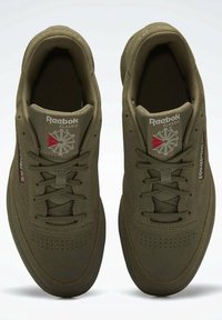 Un paio di sneakers Reebok Classic di colore verde oliva con lacci, punta perforata e logo rosso-bianco sulla linguetta, su sfondo bianco.