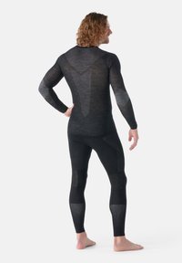 Traje de capa base en negro con texturas variadas. Cuenta con mangas largas, diseño ajustado y paneles de malla para ventilación en la espalda y los lados.