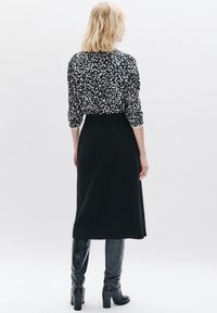 Zwarte midi-rok met een gladde, matte textuur, gecombineerd met een gebloemd blouse met witte en beige vlekken, afgewerkt met knielange zwarte laarzen.