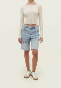 Lichte beige geribbelde langmouwen crop top gecombineerd met lichtblauwe denim shorts met een ripped detail, gedragen met witte en tan sneakers.