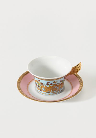 Πορσελάνινη κούπα τσαγιού με χρυσή, σχήματος φτερού, λαβή, με λουλουδάτα και σπειροειδή σχέδια σε μπλε σώμα, που στηρίζεται σε ροζ πιατάκι με χρυσό περίγραμμα.