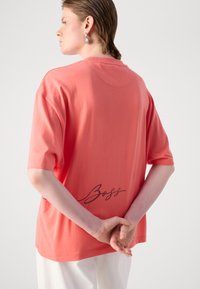 Coral oversized t-shirt made of cotton, featuring short sleeves and a rounded neckline. Text "Boss" in cursive on the back.