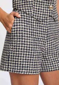 Linnen shorts in een marineblauw en crème houndstooth patroon met een gestructureerde stof, voorzien van zijzakken en een metalen knoopdetail.