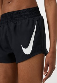 Shorts de sport noirs en matériau léger, dotés d'une taille élastique et d'un logo Nike en blanc bien visible sur le côté.