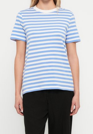 Kobieta nosząca t-shirt z krótkim rękawem i okrągłym dekoltem w poziome niebiesko-białe paski, w połączeniu z luźnymi czarnymi spodniami.