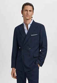 Double-breasted navy suit jacket with black buttons, notched lapels, and a white pocket square. Smooth texture, tailored fit.