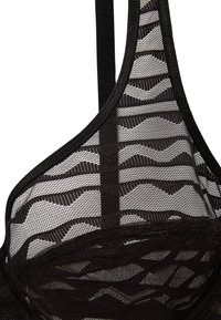 Soutien-gorge en mesh noir avec un motif à lignes ondulées. Bandes réglables douces et bords finis. Texture légère et transparente.