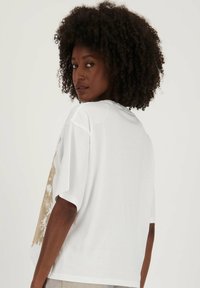 Witte t-shirt met korte mouwen en een ontspannen pasvorm, voorzien van een beige abstract ontwerp aan de linkerkant, gemaakt van zachte katoen. Gelaagde stof.