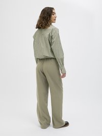 Grønn- og hvitstripet oversized skjorte med rett snitt, kombinert med løse olivengrønne bukser og svarte sko.