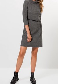 Robe en maille grise avec un col bénitier, des manches trois-quarts et une ceinture noire. Une paire de bottines noires, à texture lisse et à forme ajustée.