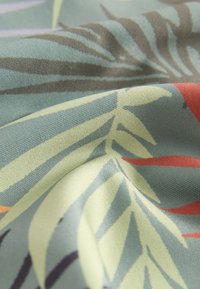 Tessuto che presenta una stoffa verde e azzurro chiaro con motivi fogliari in verde scuro, giallo pallido e accenti rossi. La texture è liscia e leggermente lucida.