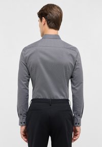 Camicia da uomo con motivo bianco e nero, maniche lunghe, colletto classico e polsini con bottoni, abbinata a pantaloni neri.