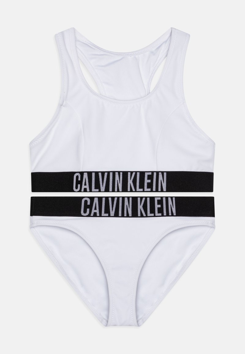 Biały strój kąpielowy składający się z topu z wycięciem na plecach i pasujących majtek. Czarne elastyczne paski z napisem "CALVIN KLEIN" w kolorze szarym, gładka faktura materiału.