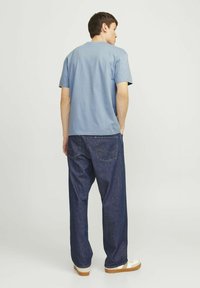 Camiseta azul claro de cuello redondo combinada con jeans de mezclilla oscuros y sueltos. La tela parece suave, con un ajuste casual y un detalle mínimo.