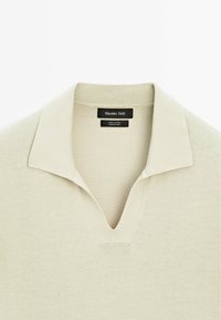 Katoenen polo shirt in lichtbeige met een v-hals, ribgebreide kraag en korte mouwen. Voorzien van merklabel aan de binnenkant van de hals.