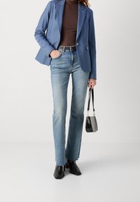 Ljusblå skräddarsydd blazer över en brun polotröja, ihopparad med ljusblå jeans och svarta ankelkängor, hållande en liten svart handväska.