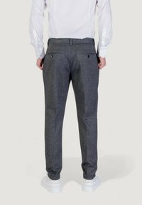 Pantaloni grigi con texture, dotati di due tasche posteriori e un fit slim, abbinati a sneakers bianche e una camicia leggera.