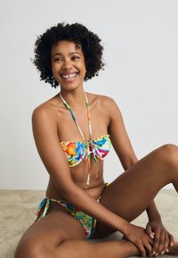 Krāsains bikini komplekts, kas sastāv no bandeau topa ar volāniem un regulējamiem saitēm, kas saskaņots ar sānos saistāmiem apakšbikiniem ar ziedu rakstu.