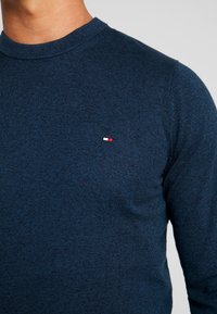 Suéter azul marino hecho de tejido de punto texturizado, con cuello redondo y un pequeño logo en rojo, blanco y azul en el pecho.