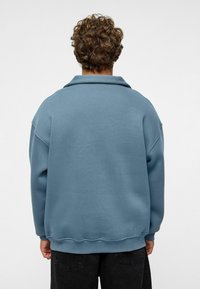 Overmaatse blauwe sweatshirt met een brede kraag, verlaagde schouders en een ribbelzoom. Zachte textuur, minimalistisch ontwerp, geen zichtbare patronen of hardware.