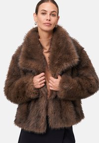 Manteau en fausse fourrure marron avec un large col, un design court et des manches longues. Texture douce, apparence touffue et ajustement snug autour du corps.