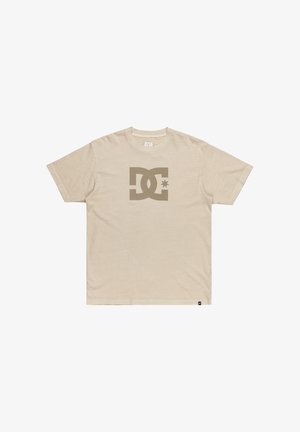Camiseta de algodón beige con un gran logo de DC en un beige oscuro y una estrella en el frente. Mangas cortas, cuello redondo y ajuste estándar.