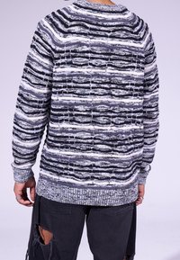 Strickpullover mit strukturiertem, gestreiftem Muster in Schwarz und Weiß. Verfügt über einen Rundhalsausschnitt und gerippte Bündchen, angepasst für einen lässigen Schnitt.