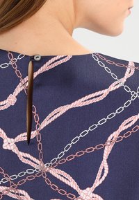 Top de tela azul marino con un diseño de apertura en la parte posterior, que presenta un patrón de cuerda y cadena en rosa y blanco, terminado con un cierre de botón.