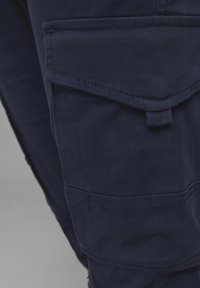Marinblå cargobyxor i bomullsmaterial med en texturerad yta, som har en stor klaffficka och en tab för justeringar.