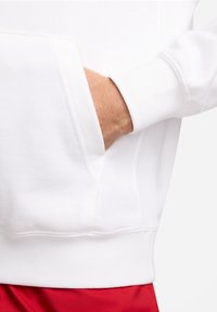 Vit sweatshirt med en framficka, synliga sömmar och ribbade muddar. Materialet verkar mjukt och slätt, framhävt av en avslappnad passform.