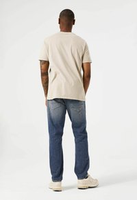 Camiseta de algodón beige de manga corta, combinada con jeans de denim azul. El conjunto presenta un corte relajado y un diseño sencillo, con costuras traseras visibles.