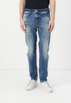 Jean en denim bleu clair au fit décontracté, comportant cinq poches, un léger délavage et une coupe droite, associés à des baskets blanches.