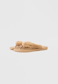 Brune flip-flops med myke plysjstropper, en teksturert såle og et sporret yttersåle; har en gulllogo som aksent på stroppen.
